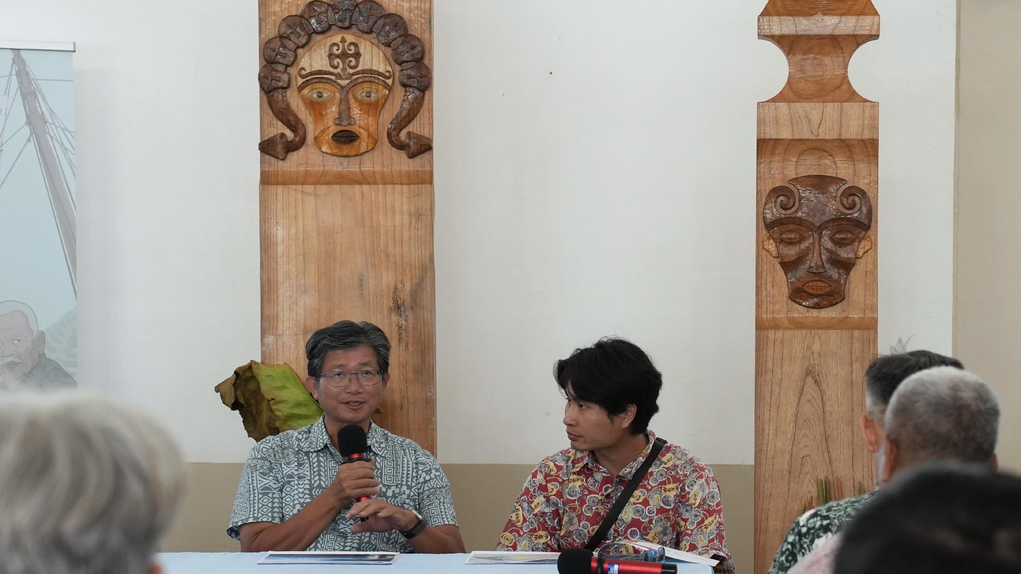Speaker presenting on pottery revival between Taiwan and Palau in front of carved wooden Palauan panels, September 2026