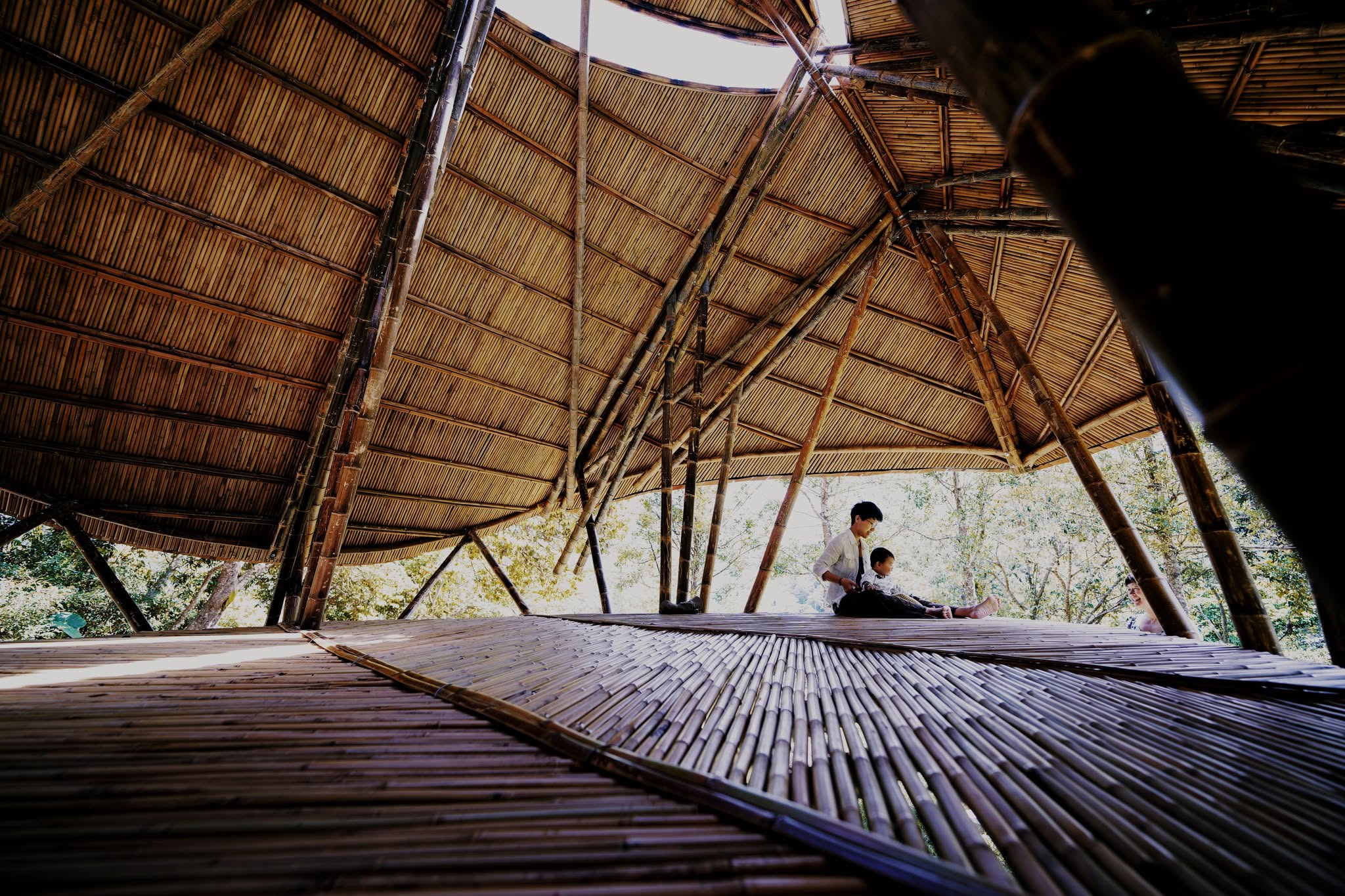 Visitors sitting inside a bamboo pavilion, looking up at its woven bamboo roof structure, Taitung