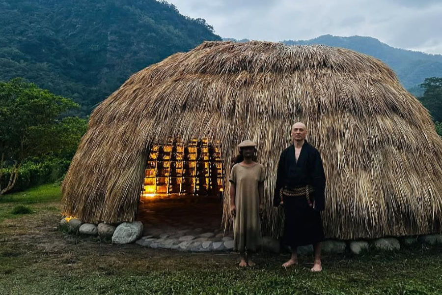 Two people standing in front of the completed thatched bamboo dome structure at dusk, Taitung