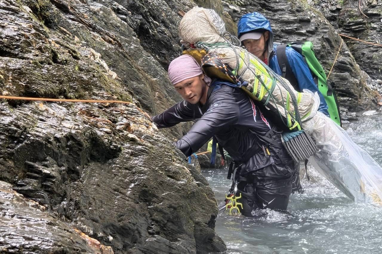 重い荷物を背負い、渓流沿いの岩壁を登る高山ルートのガイド