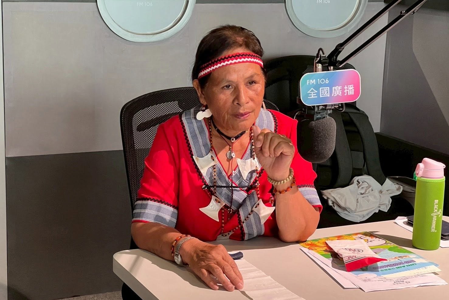 Sinan Jiotok speaking in a radio studio while holding a woven strip