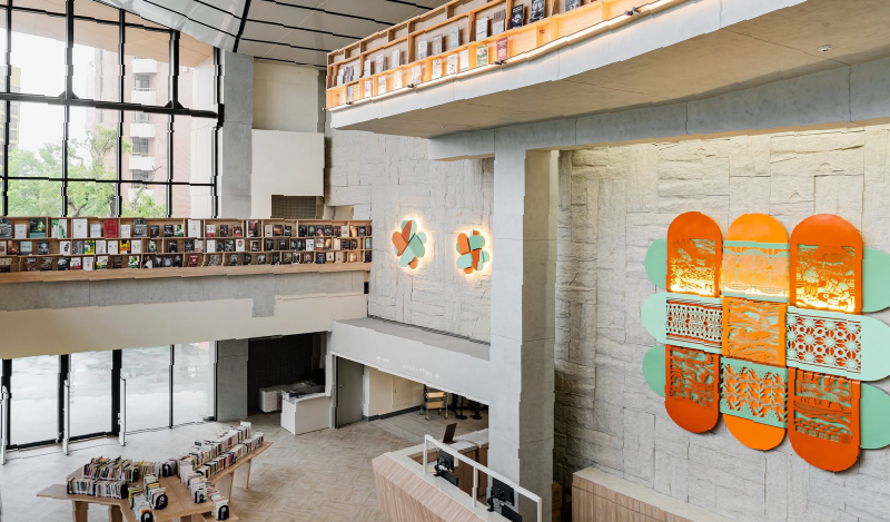 Library atrium with a wooden bookshelf gallery and a large orange and green decorative panel on a stone wall